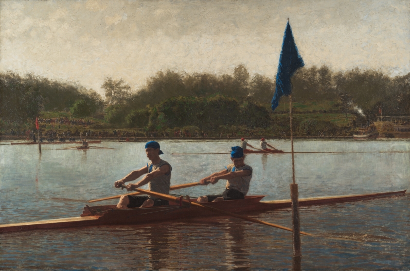 An oil painting showing a scene from a rowing competition on a river. In the foreground, two men are in an long rowboat, having just manuevered around a stake planted in the riverbed. The two men are wearing dark blue bandanas on their heads, the colors of which match the flag atop the stake. In the middleground, another team of rowers, wearing bright red bandanas, are approaching their stake. In the background, a large riverboat and smaller ship are anchored near a wooded shore under a cloud-filled sky, densely populated with spectators. Other than the bandanas and flags, the colors of the painting are all grays, greens and browns.