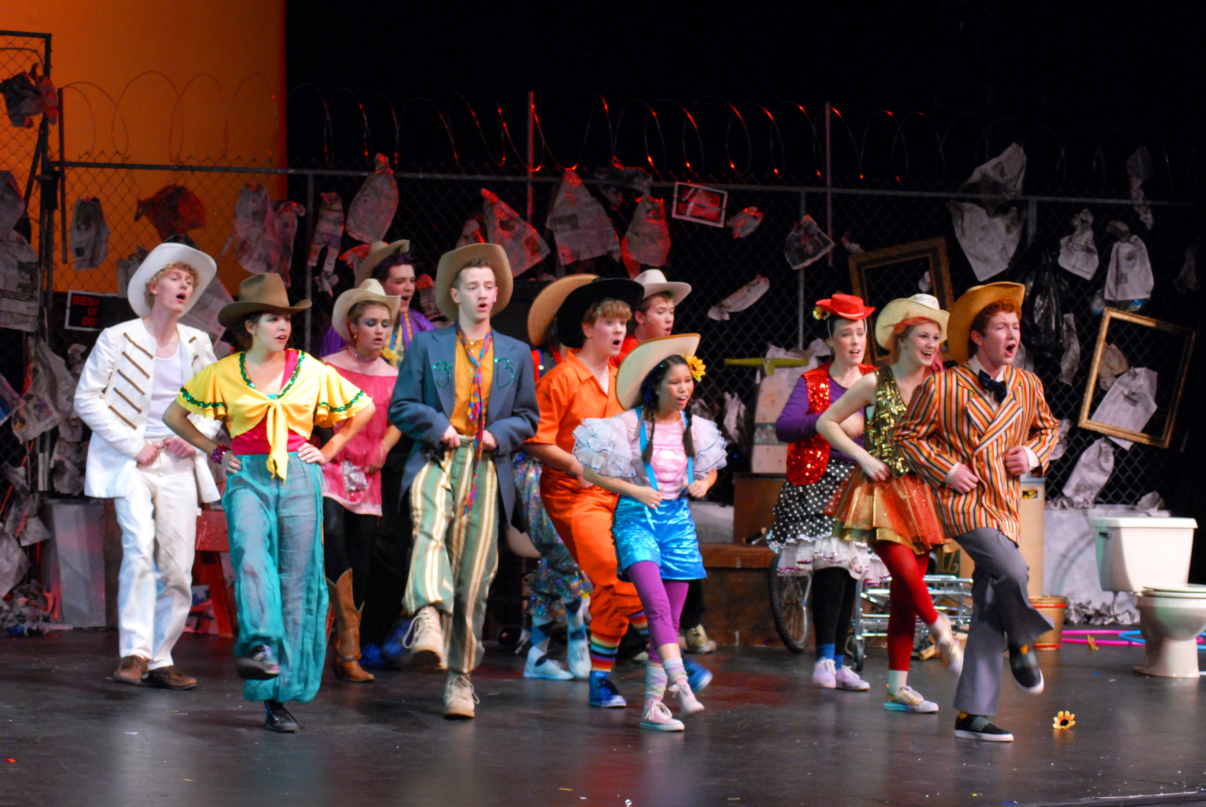 Eleven student performers wearing wildly colorful and mismatched clothes dance in formation.
