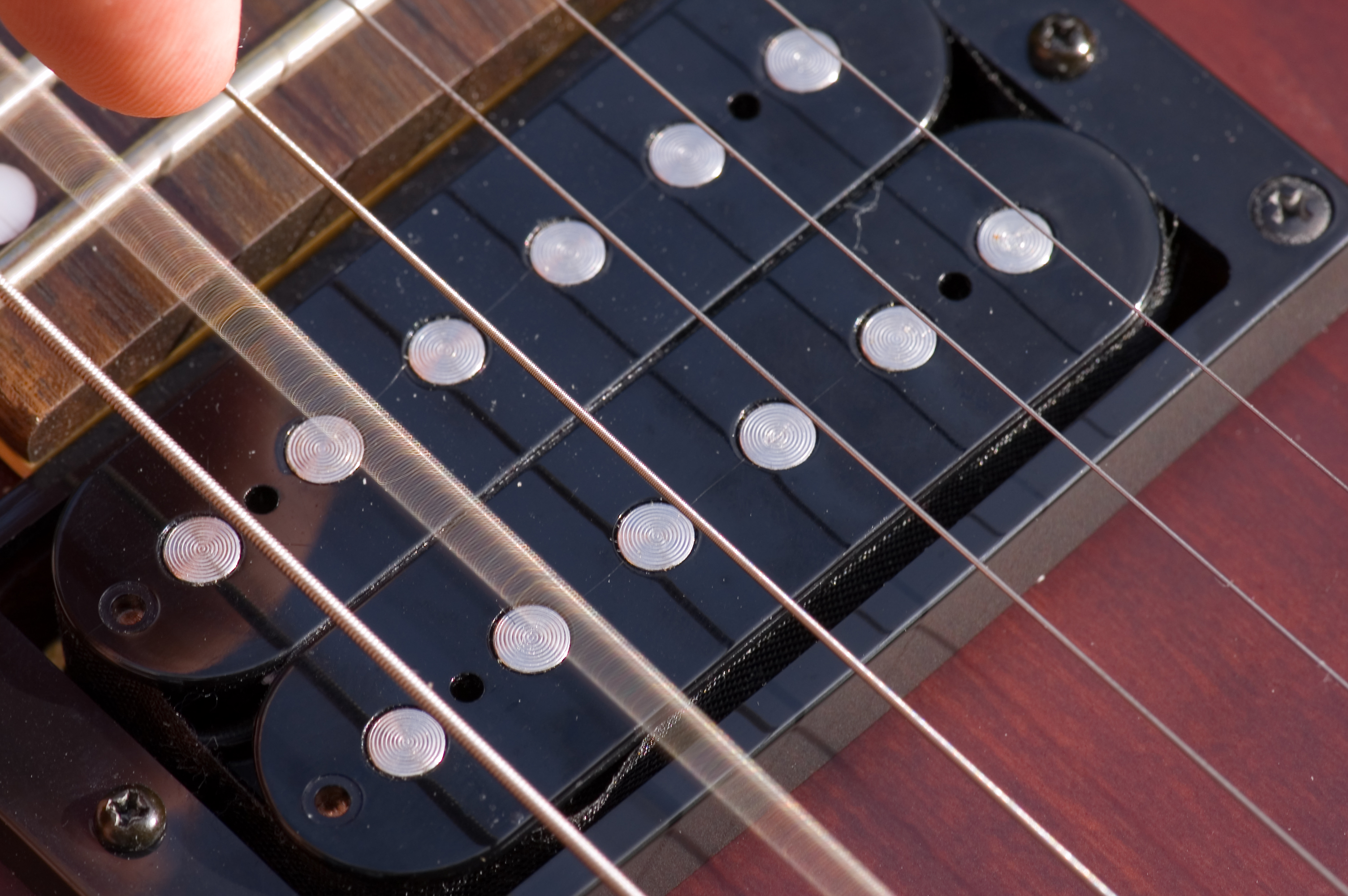 A close-up photograph of an electric guitar, showing two sets of pickups underneath the strings. The flat ends of the cylidrical metal pickups are set flush with the surface of black metal housing; ends of the pickups themselves have slight concentric circular ridges. In the photograph, the second string is blurred, having just been plucked.