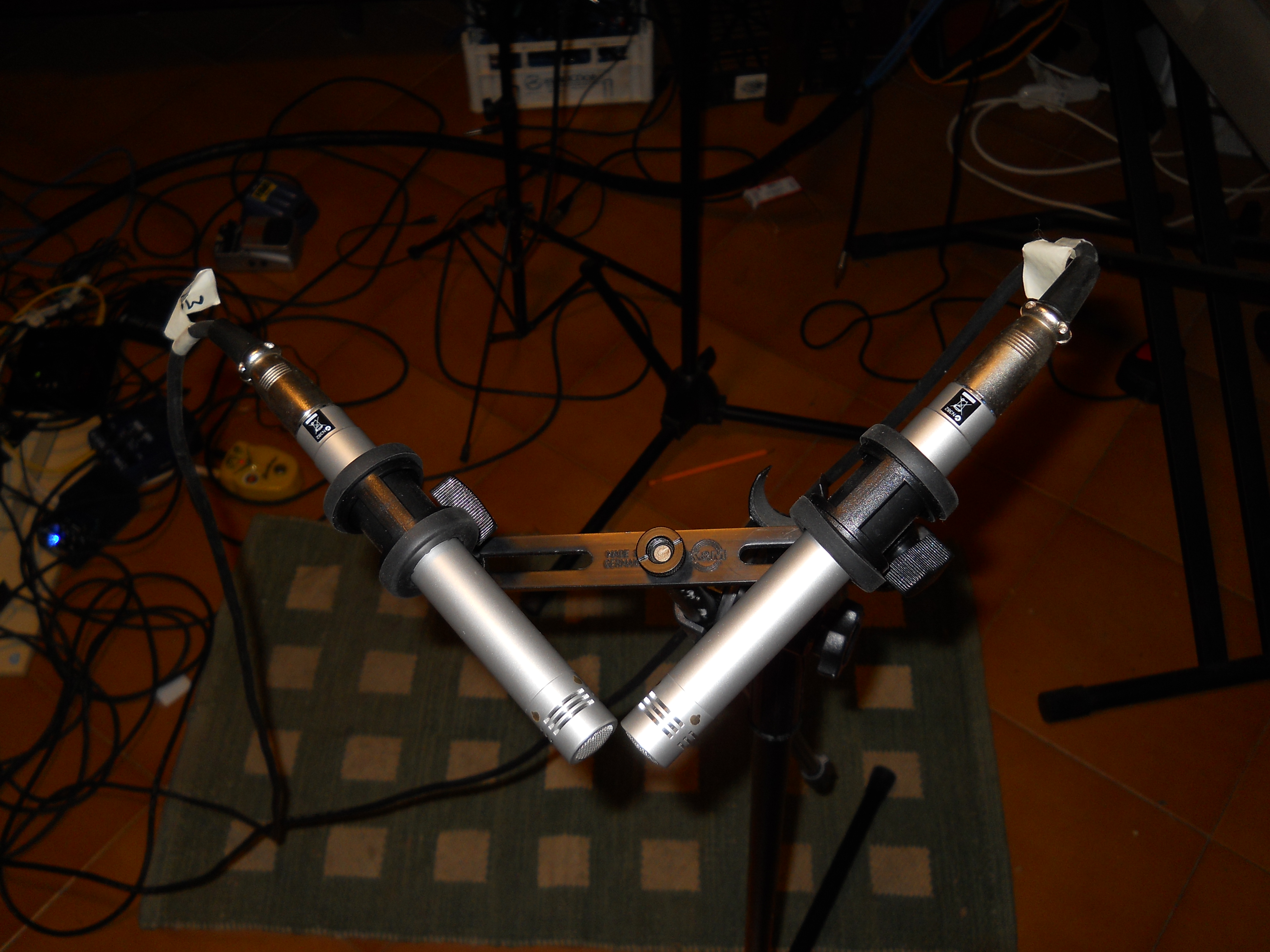 A photograph from above of two microphones held in place with a bracket. The microphones are long and cylindrical and placed so that the mesh end of each microphone is placed 90 degrees from one another, with the edges of the microphones almost touching.