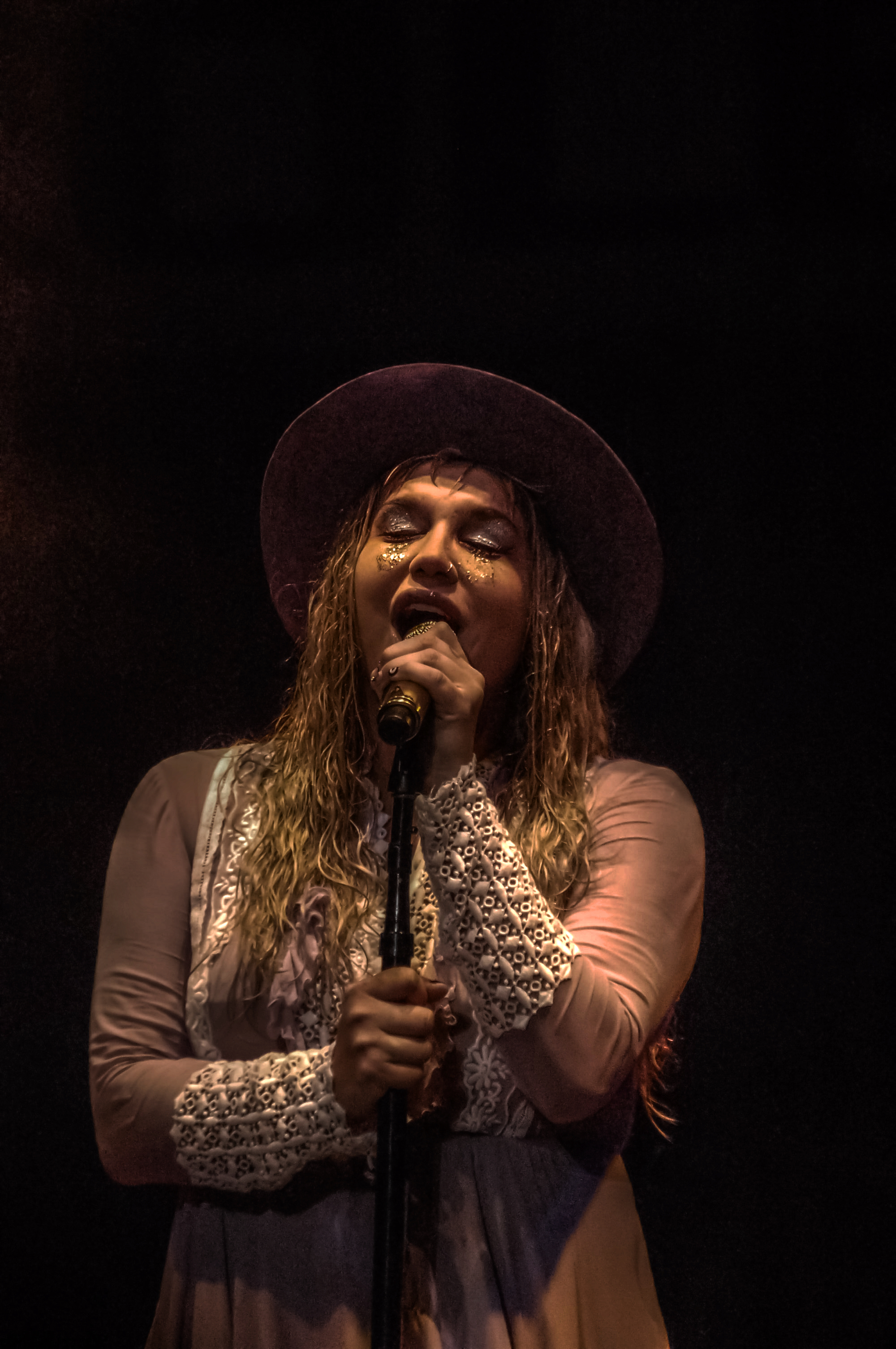 Kesha Sebert singing into a microphone against a black background.