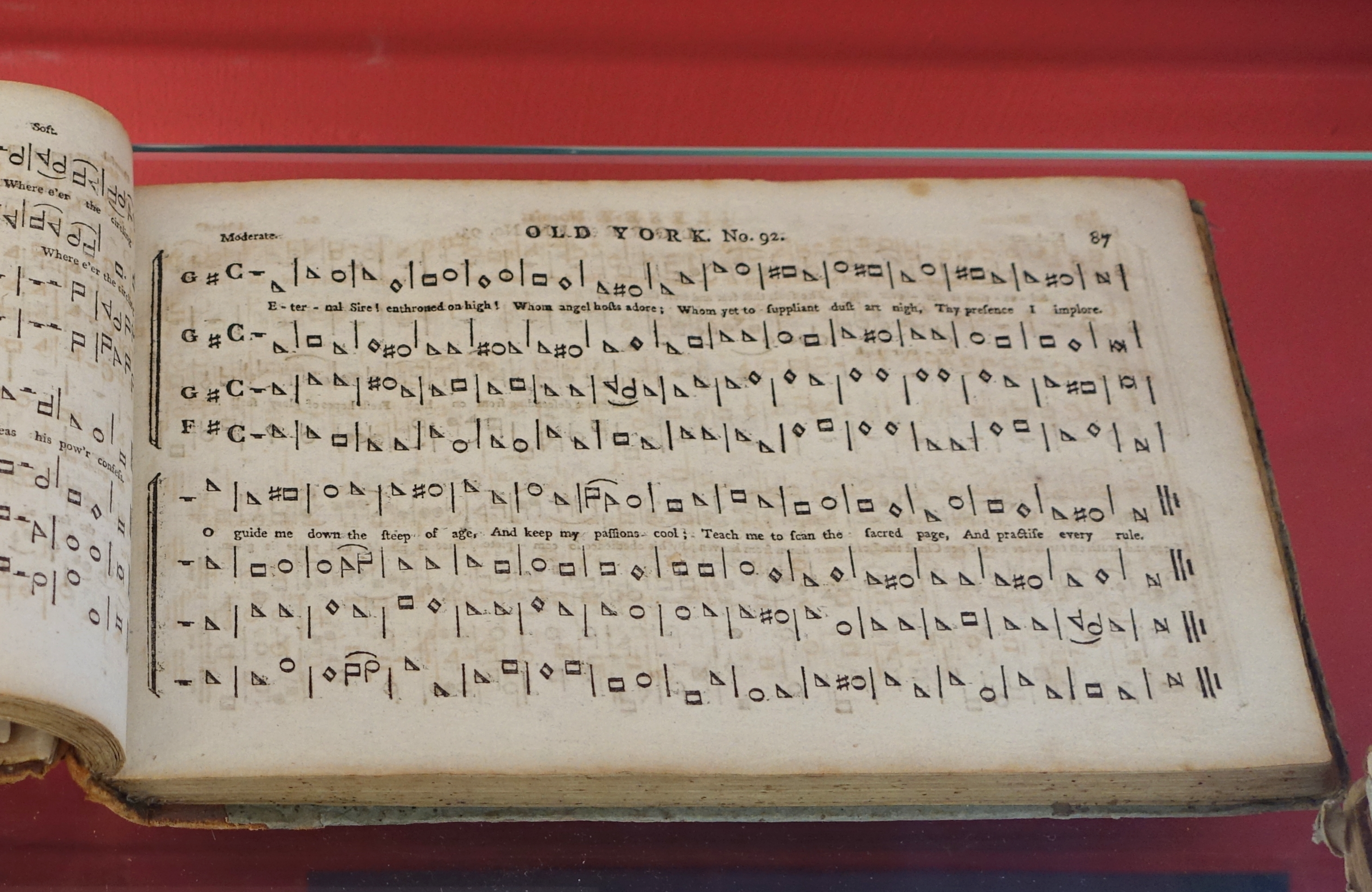 An old, yellowed book of music opened to a page with the heading `Old York, No. 92`. The music is a four-part score in two systems with lyrics printed under the top part. Each part is shown without staff lines, and with notes in the shape of rectangles, triangles, ovals and diamonds.