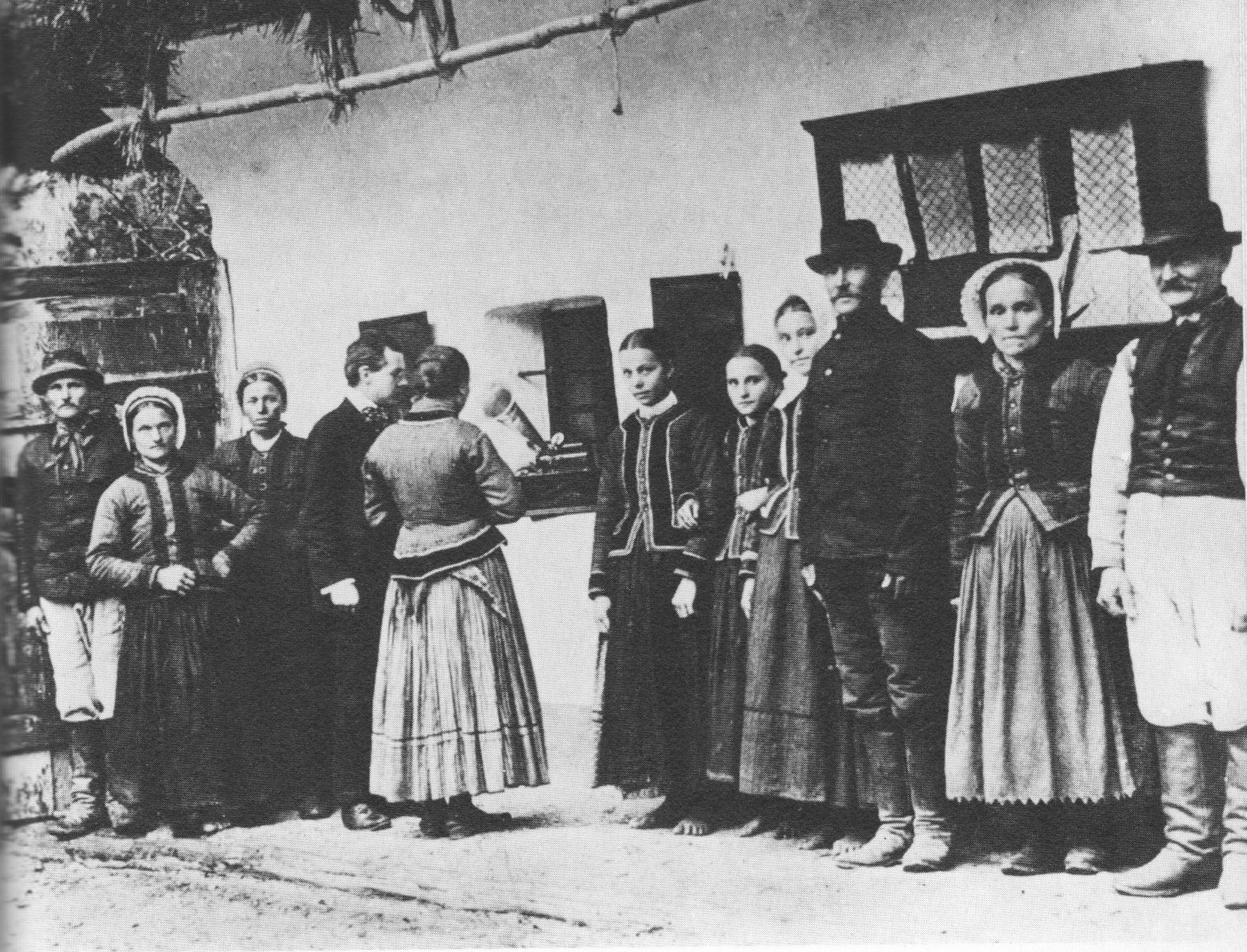 A photograph of composer B&eacute;la Bart&oacute;k using a phonograph to record a Slovak woman singing a folk song, outdoors in a rural village, while other townspeople stand attentively nearby.