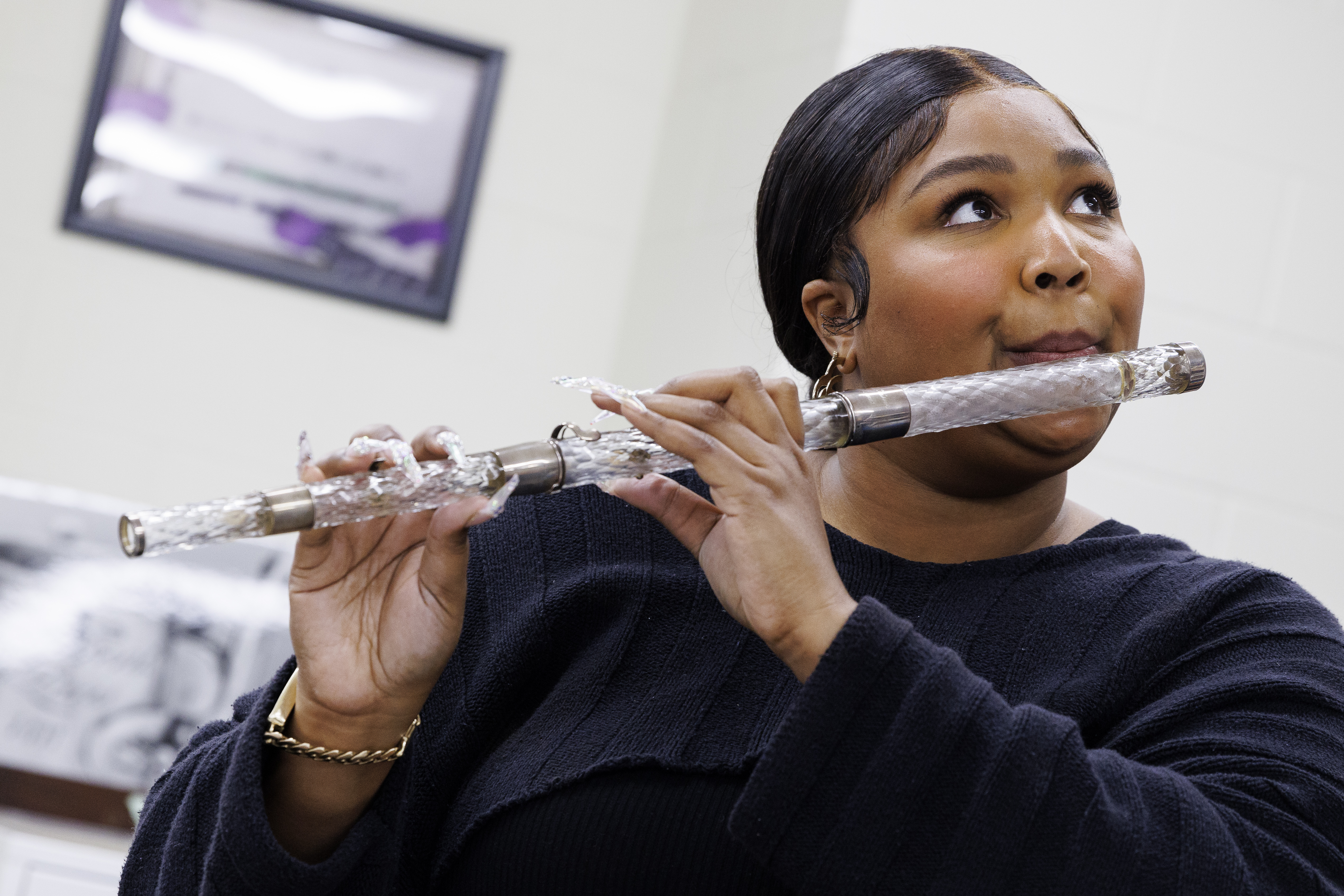A near-field photograph of Lizzo playing a flute which is made from patterned crystal with metal joints in one of the holding rooms at the Library of Congress.