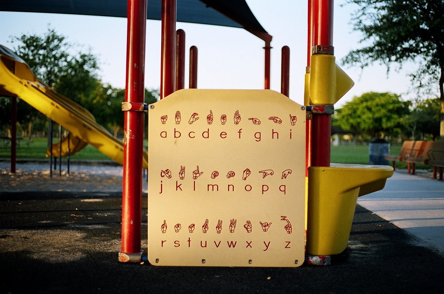 A photograph of a large placard on an outdoor playground showing the letters of the alphabet with their corresponding symbols in American Sign Language.