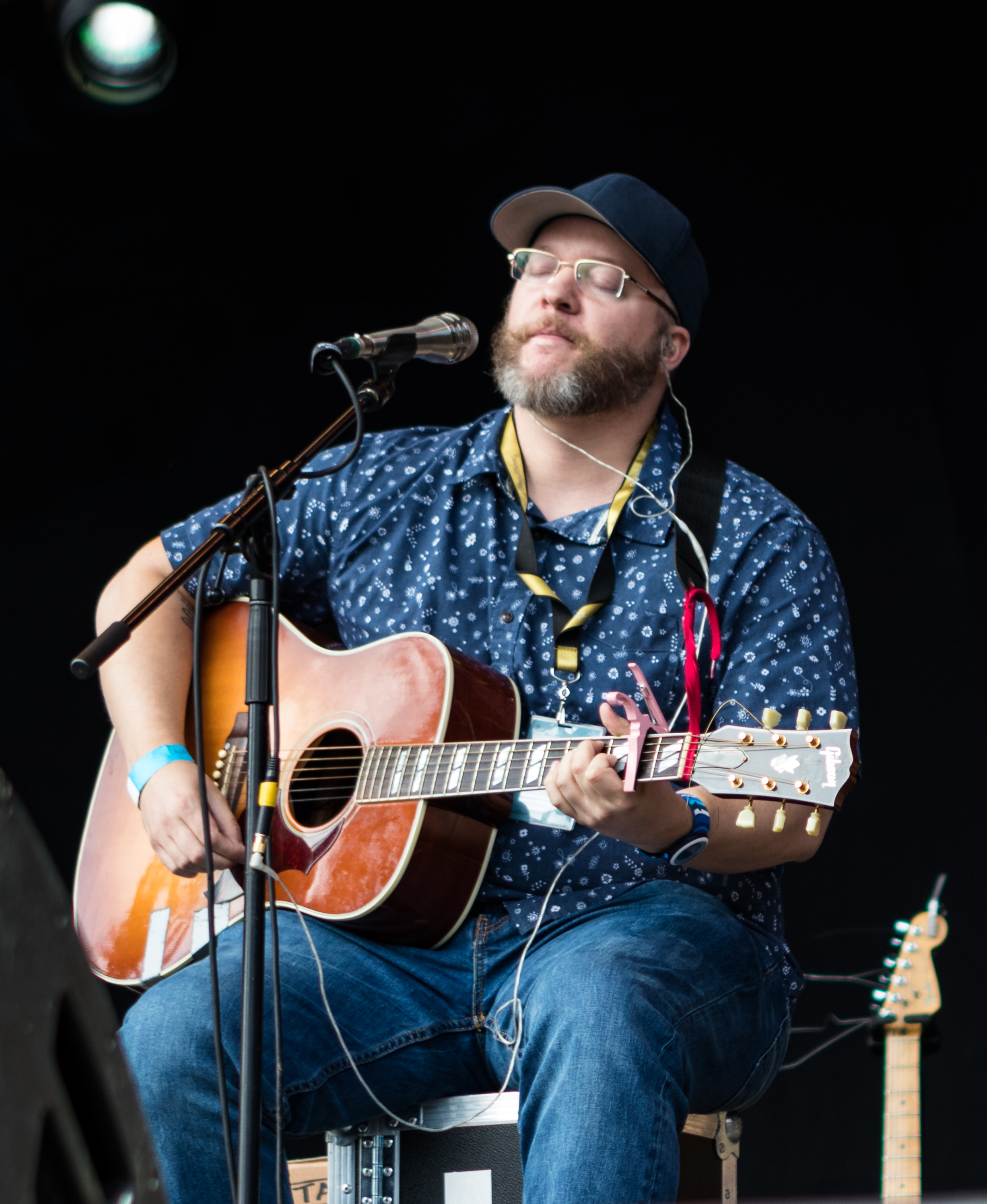 A photograph of Ben Cooper, playing an acoustic guitar while seated on stage.