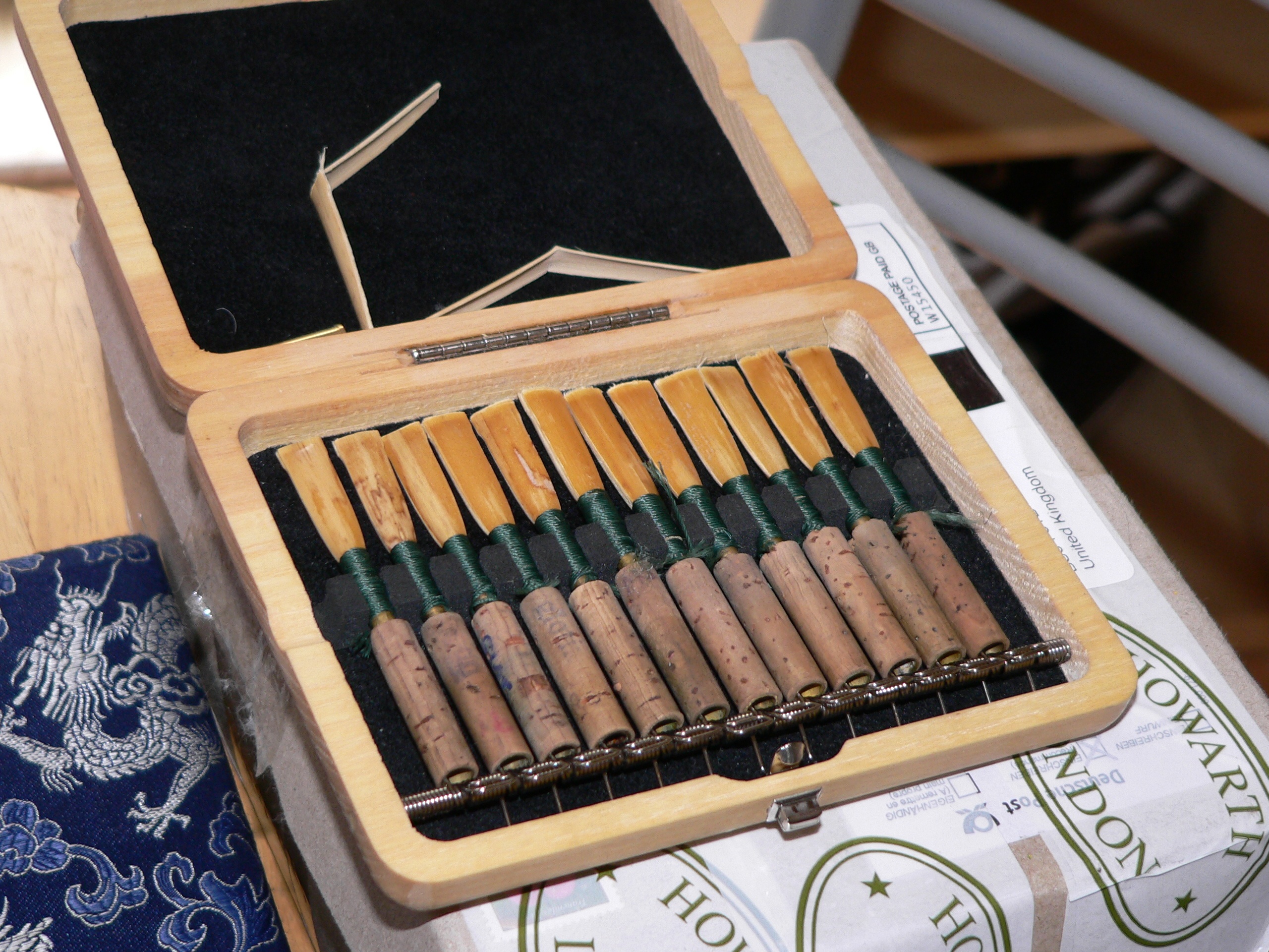 A folding wooden box containing 12 oboe reeds and two uncut pieces of cane.