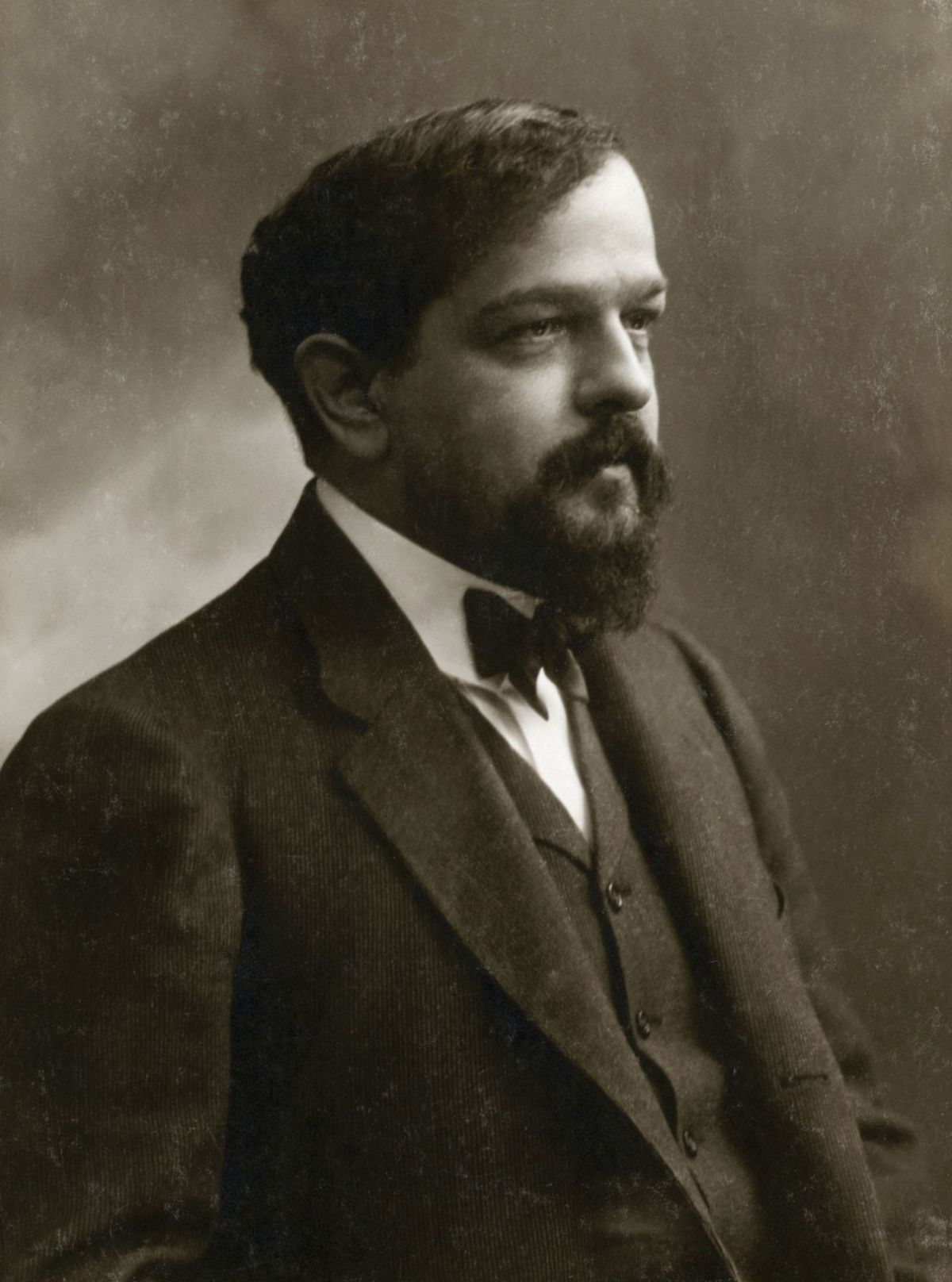 A black and white photograph of Claude Debussy, wearing a three-piece suit, a goatee and mustasche.