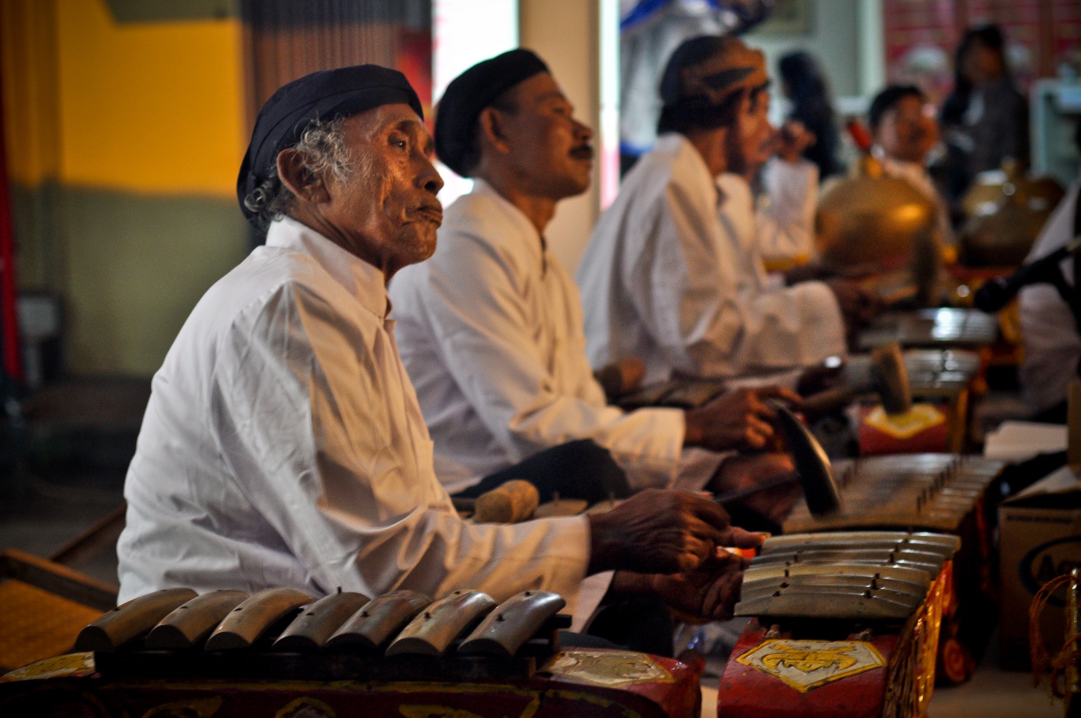 Several men seated behind ornately decorated metallophones, playing them with hammers.